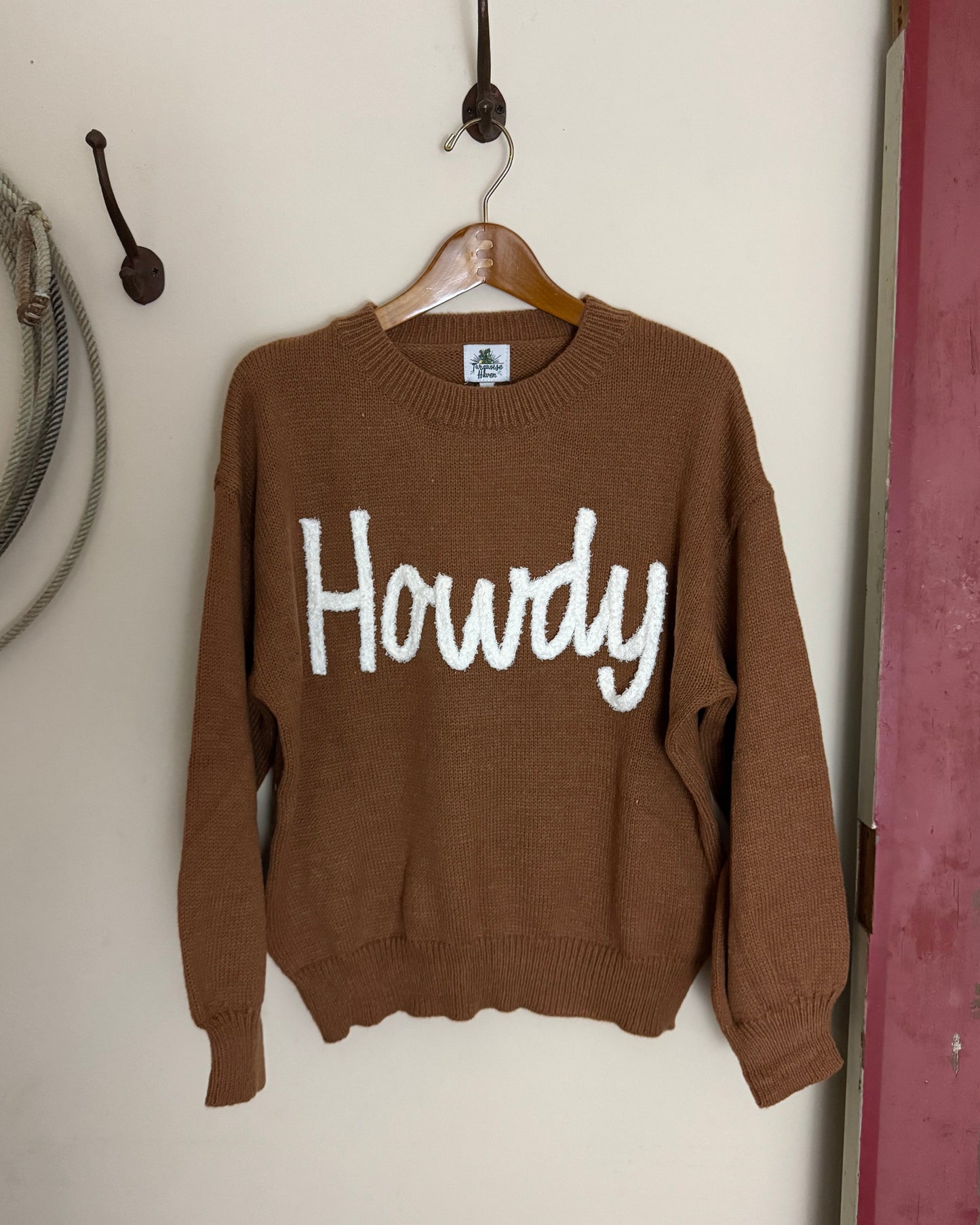 Brown sweater with 'Howdy' text on a white surface