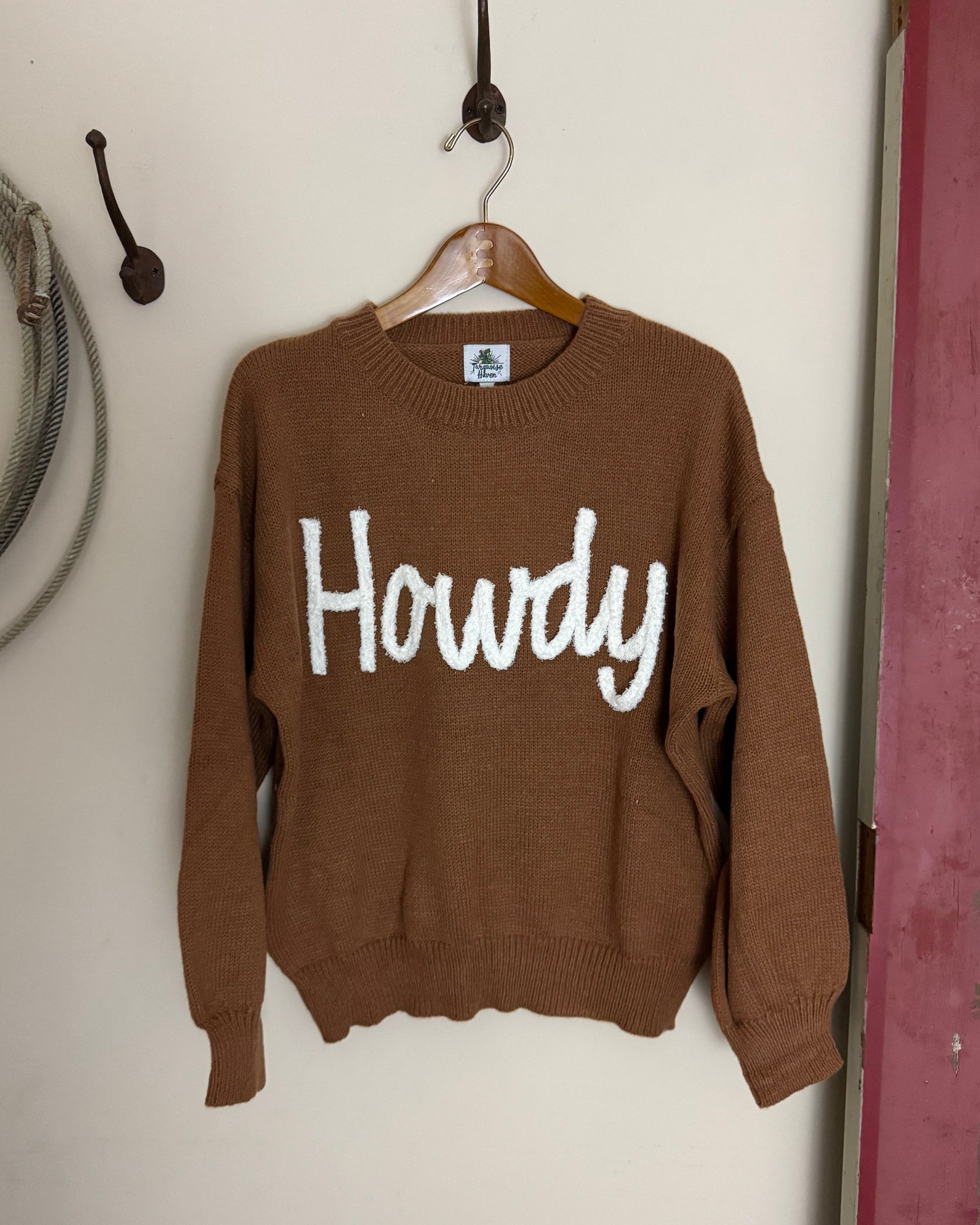Brown sweater with 'Howdy' text on a white surface