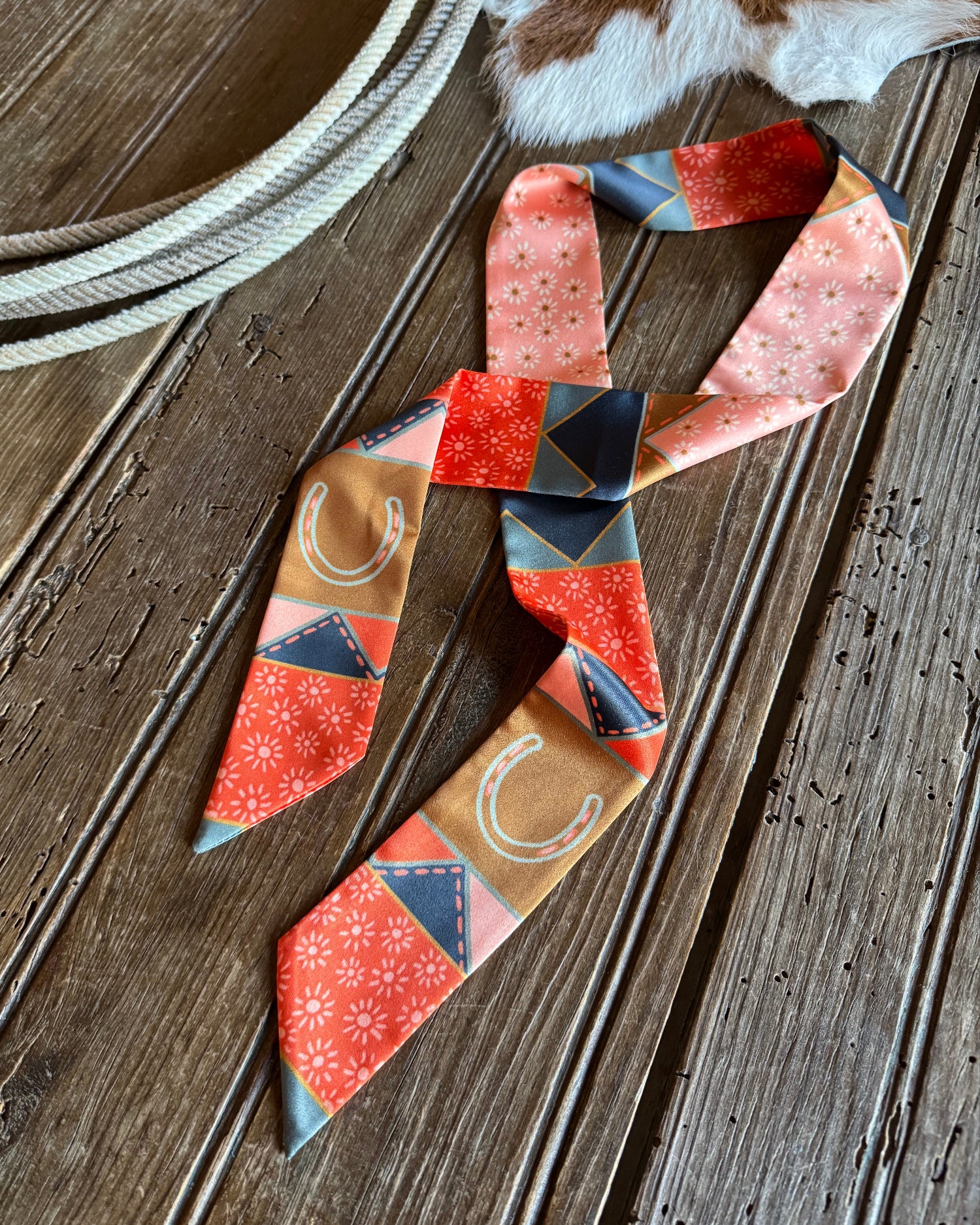 Quilt patchwork twilly scarf on a rustic wooden background with a cowhide and a rope