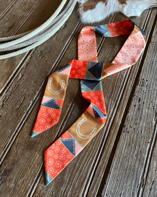 Quilt patchwork twilly scarf on a rustic wooden background with a cowhide and a rope