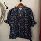 Navy floral blouse on a wooden hanger against a white wall.