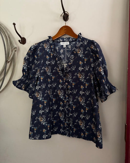 Navy floral blouse on a wooden hanger against a white wall.