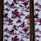 A close-up of a fabric product featuring a classic purple and white toile de Jouy pattern with riders and trees, framed by dark brown wooden slats.