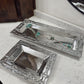 Two silver jewelry trays on a marble surface with a wooden cabinet in the background.