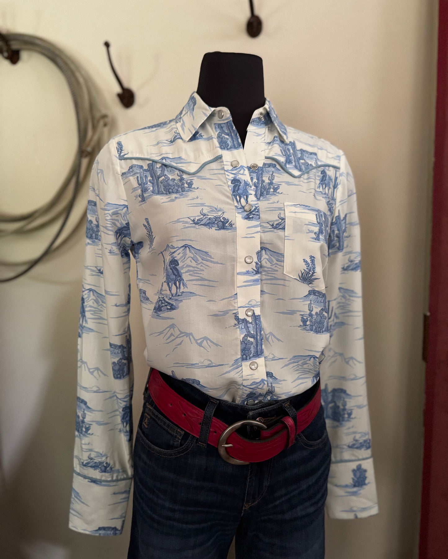Mannequin wearing a white shirt with blue patterns and dark jeans against a neutral background
