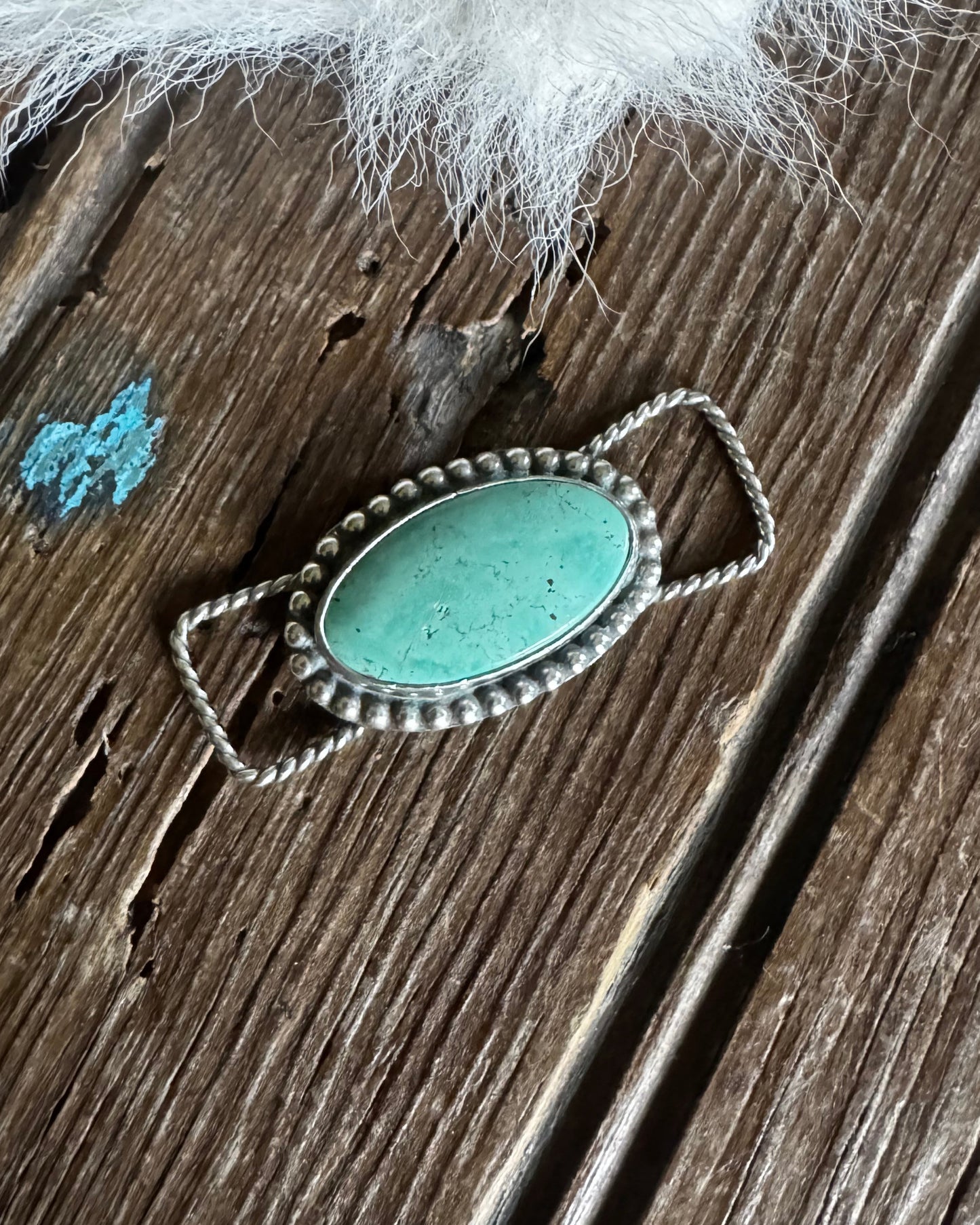 Turquoise stone ring on a wooden surface with white fur