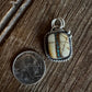 Silver pendant with a stone on a wooden surface next to a coin for scale.