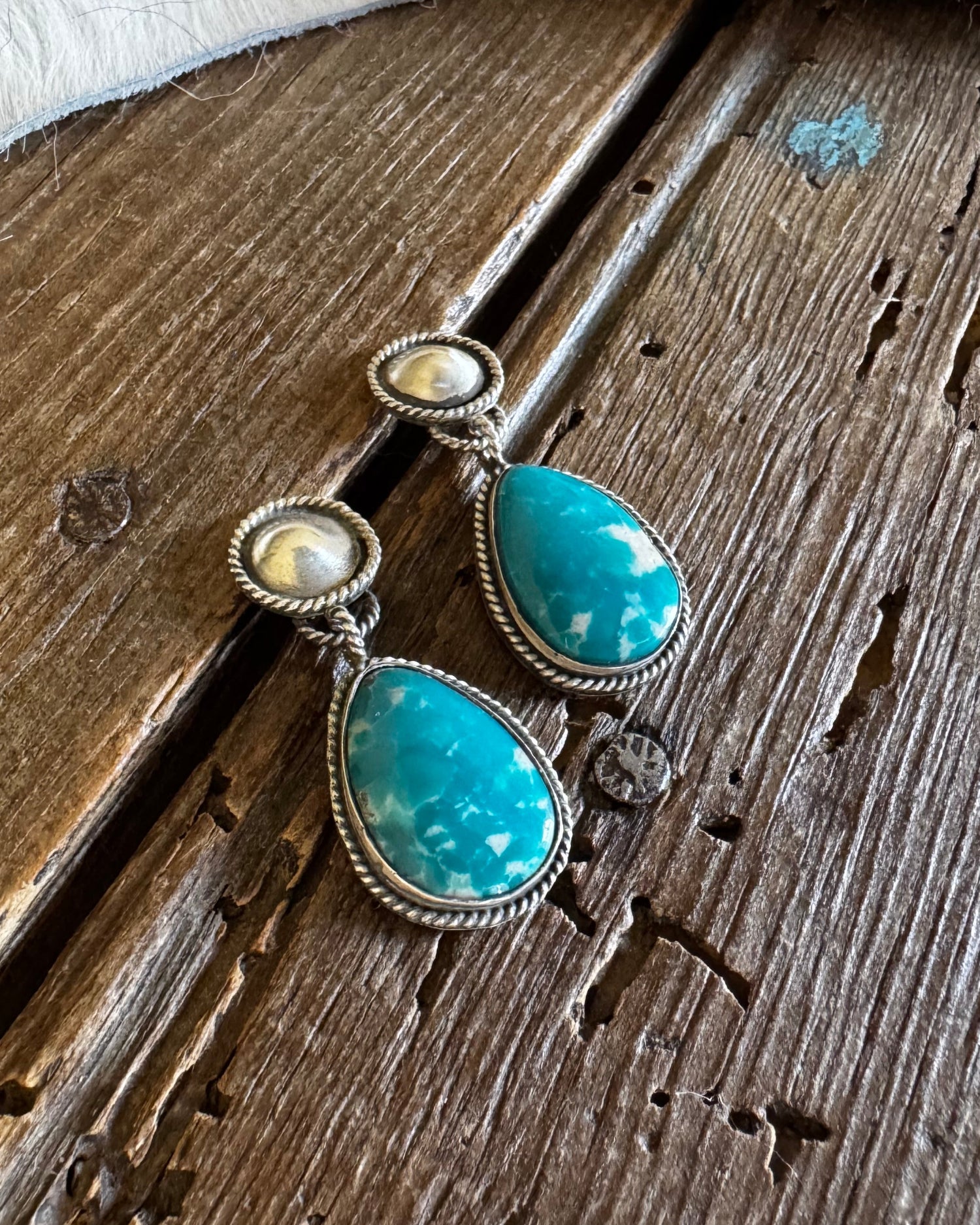 Turquoise earrings with silver accents on a wooden surface