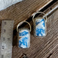 Two matching rectangular pendant earrings with blue and white marbled inlay and silver-tone metal frames, displayed on a rustic wooden surface next to a metal ruler for scale.