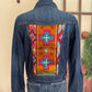 Denim jacket with a colorful geometric pattern on the back, displayed against a neutral wall.