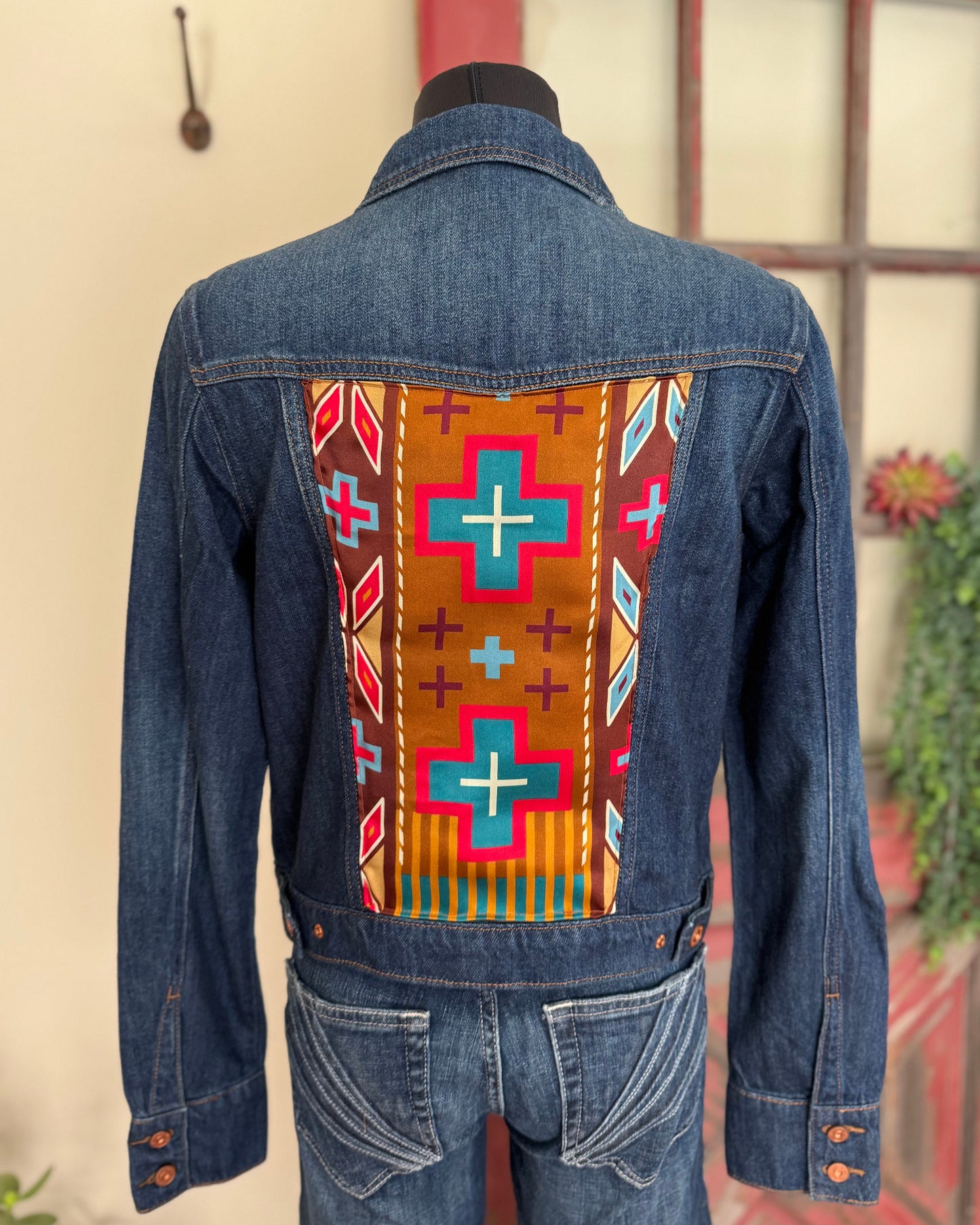 Denim jacket with a colorful geometric pattern on the back, displayed against a neutral wall.