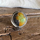 A round clear resin ring holder or coaster featuring a split design of vibrant orange-yellow and dark black, resting on a rustic wooden surface.