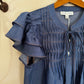 Blue shirt with ruffled sleeves on a hanger against a beige wall