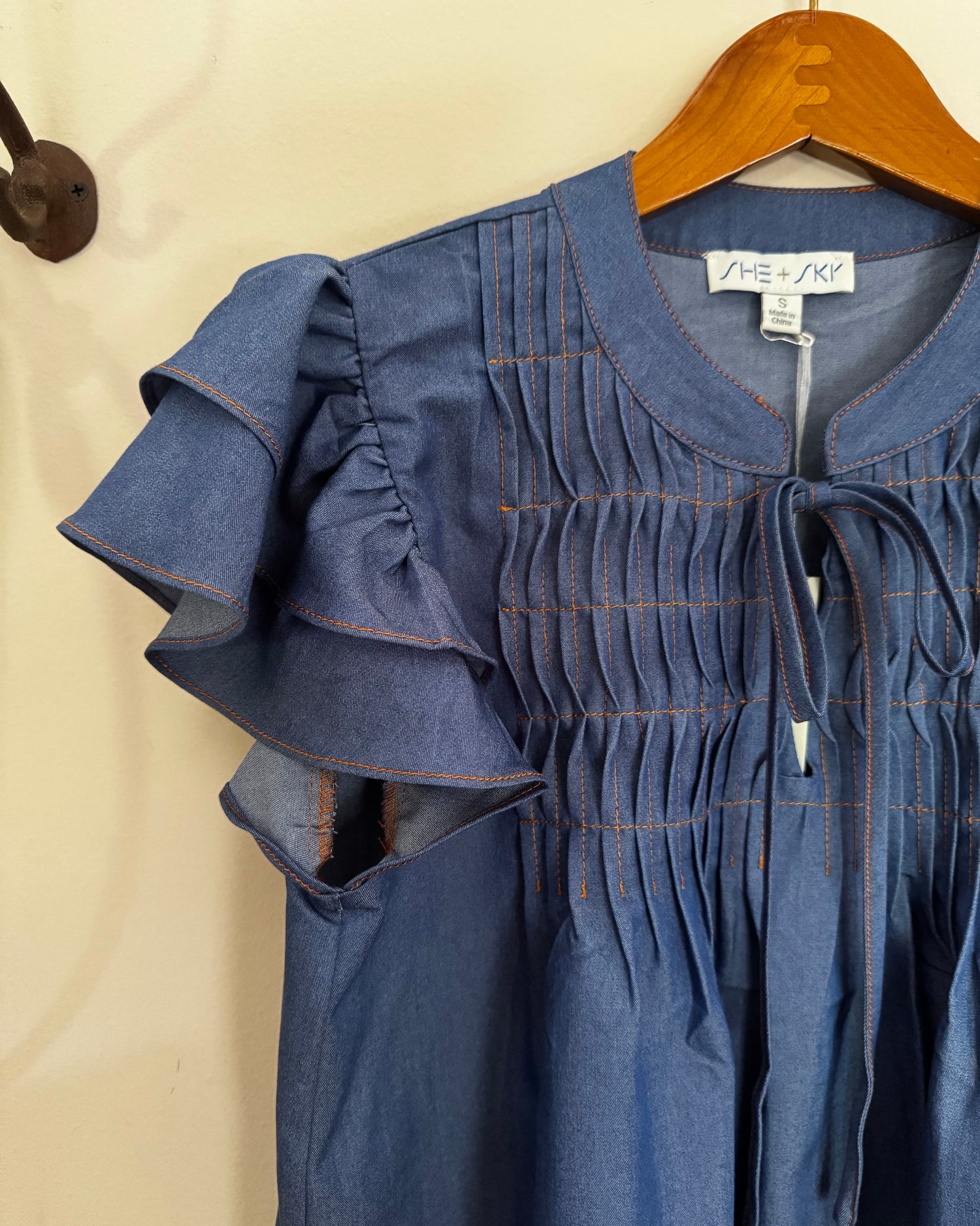 Blue shirt with ruffled sleeves on a hanger against a beige wall