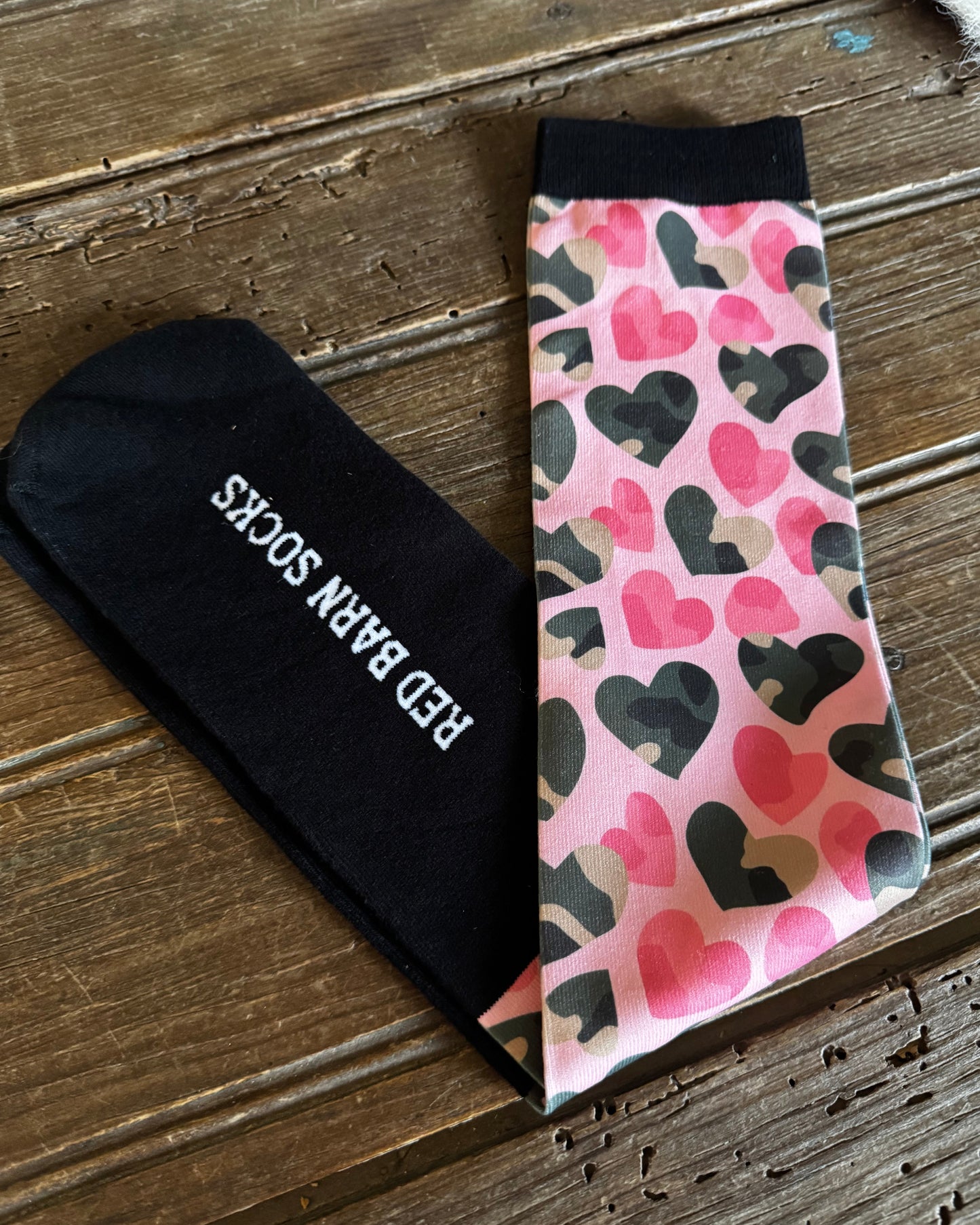 Black sock with 'Red Baron Socks' text and patterned pink tie on wooden surface