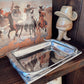 Silver tray on a wooden surface with a book and decorative items in the background