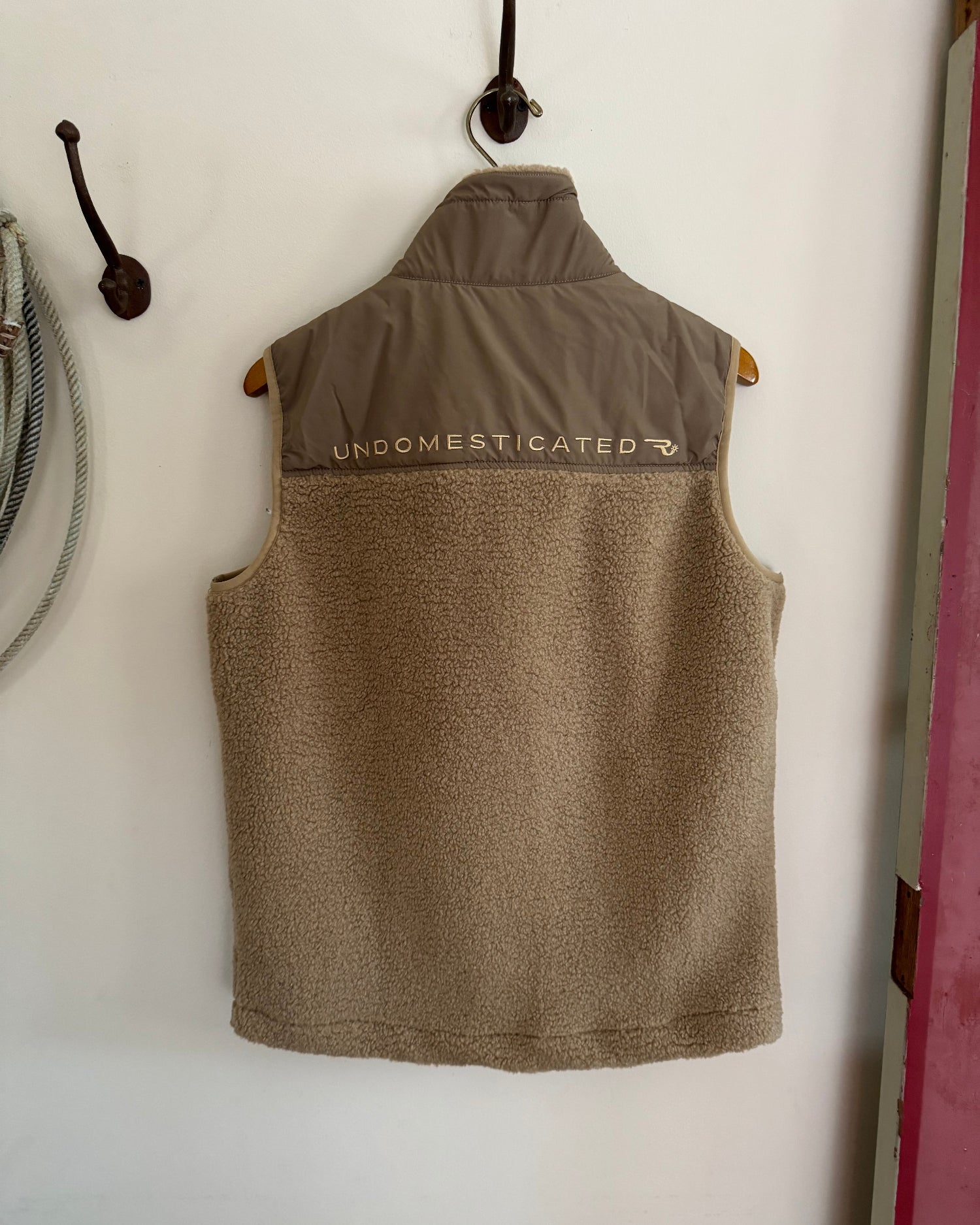 Brown vest with 'UNDOMESTICATED' branding on a white wall.