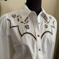 White shirt with black embroidery on a mannequin against a beige wall.