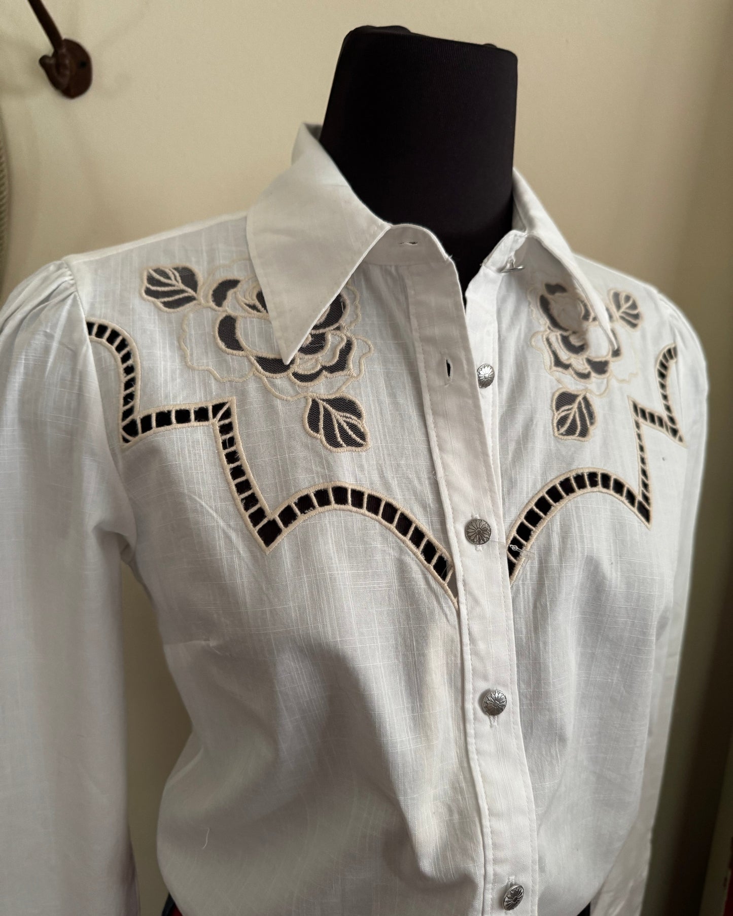 White shirt with black embroidery on a mannequin against a beige wall.