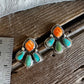 A pair of silver stud earrings with orange cabochon and turquoise inlay, displayed on a rustic wooden surface next to a metal ruler for scale.