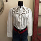 White blouse with black embroidery on a hanger against a neutral background