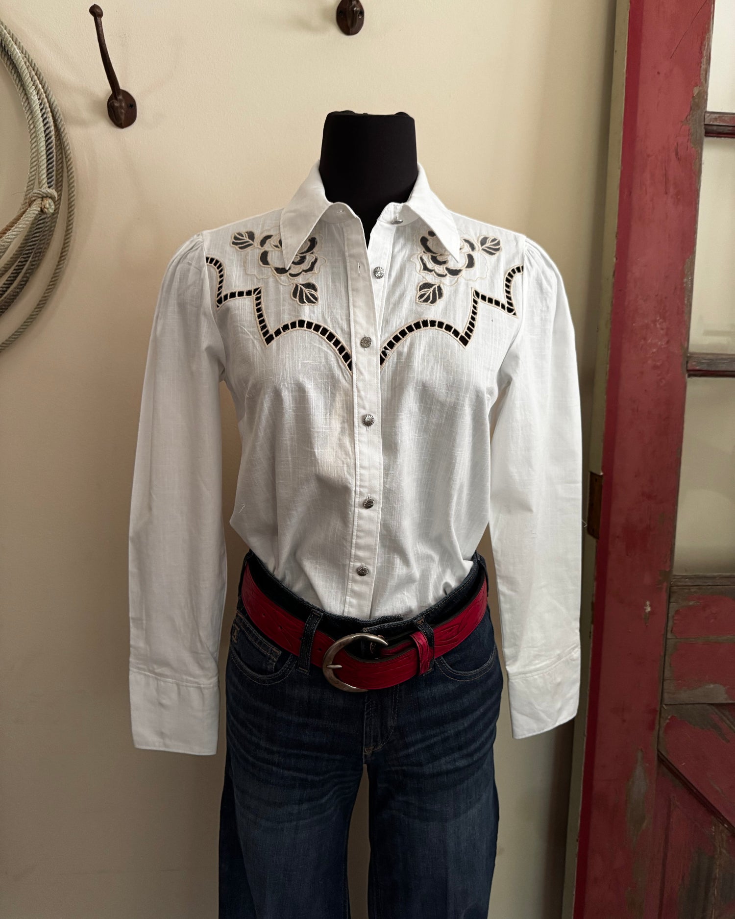 White blouse with black embroidery on a hanger against a neutral background