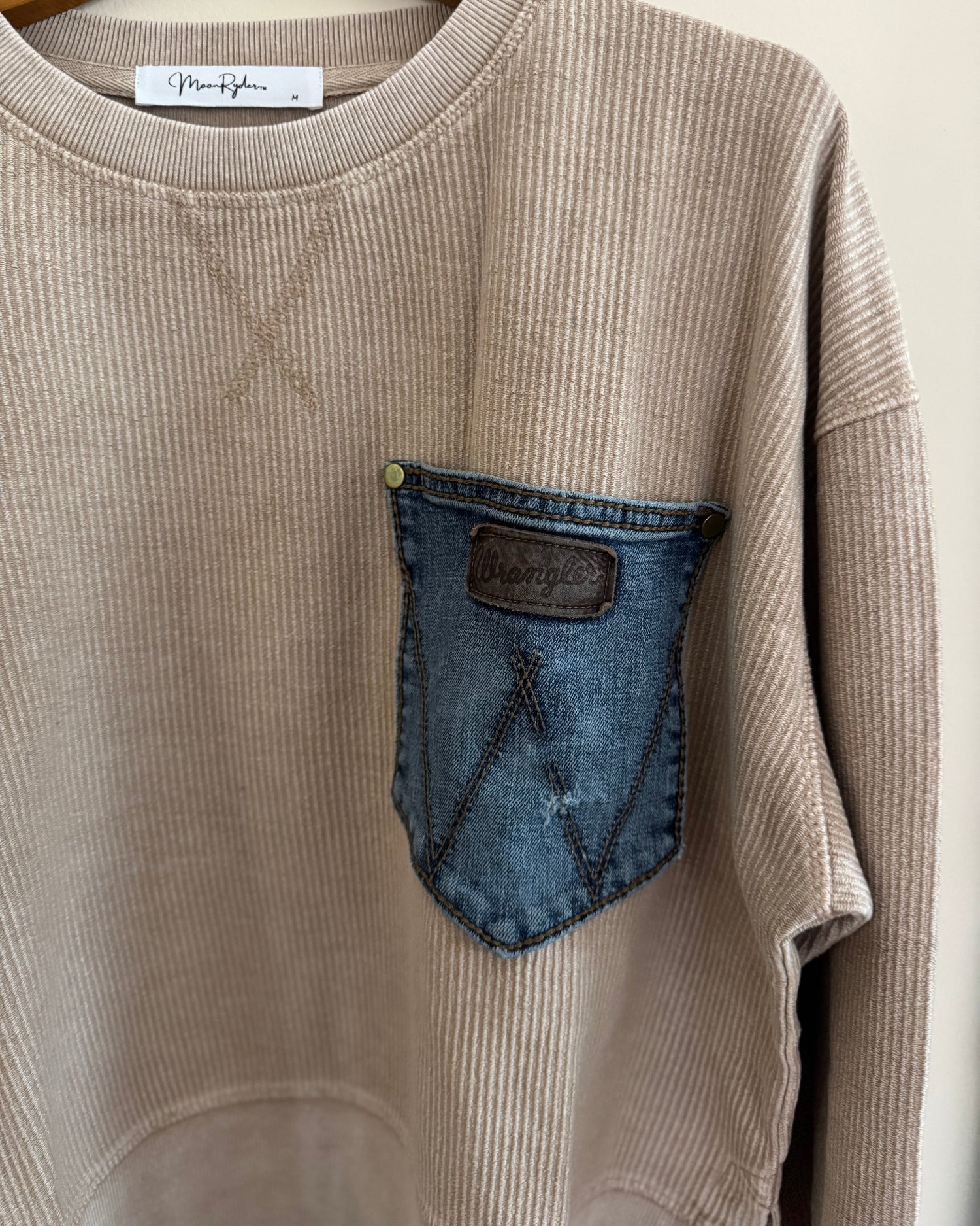 Beige sweatshirt with a denim pocket patch on a hanger
