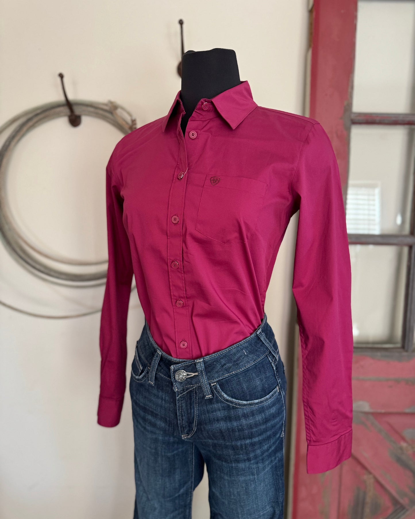 Pink shirt and blue jeans on a mannequin against a neutral wall.