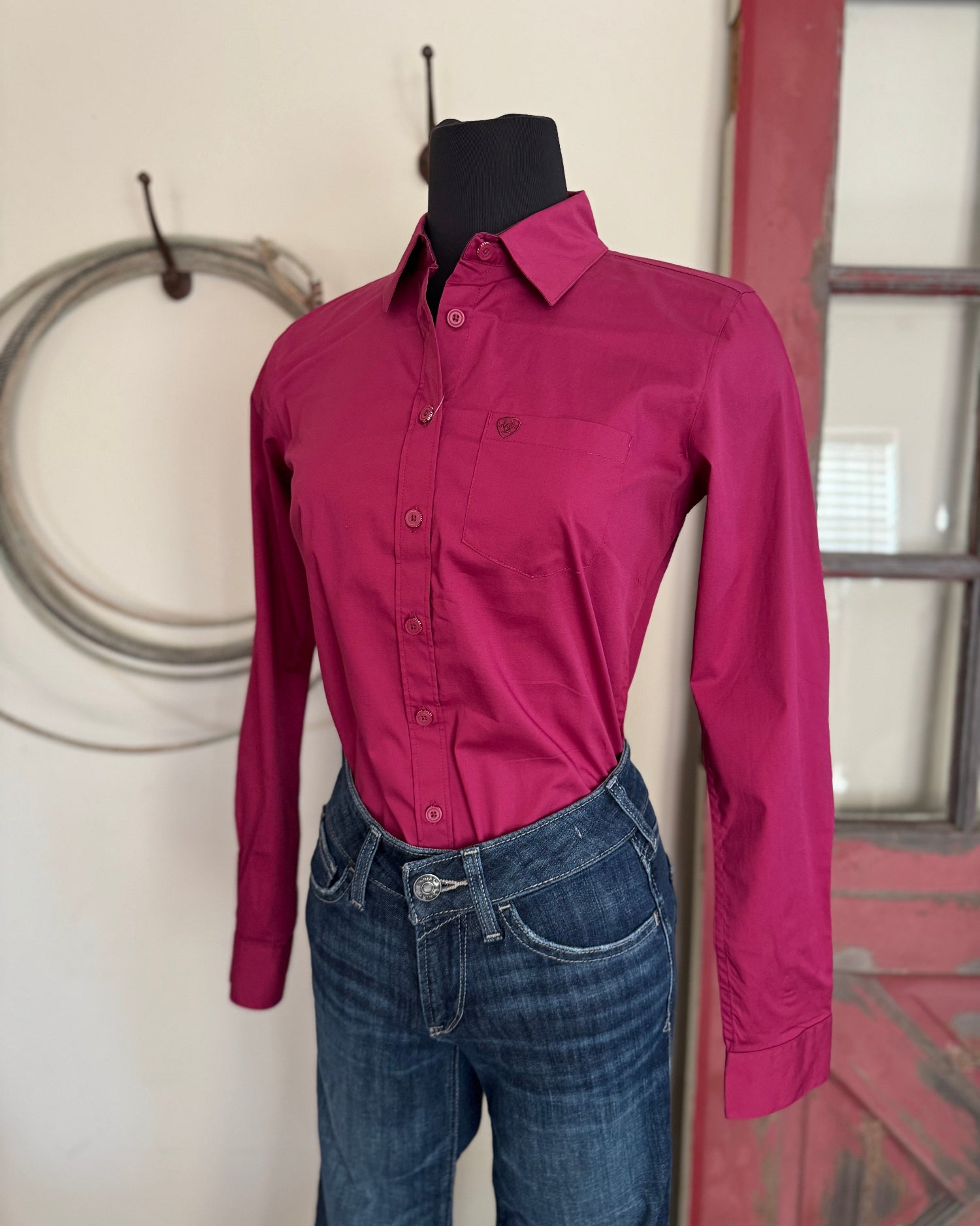 Pink shirt and blue jeans on a mannequin against a neutral wall.