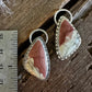 A pair of teardrop-shaped dangle earrings with pinkish-brown and cream marbled stones in silver bezel settings, displayed on a rustic wooden surface next to a metal ruler for scale.