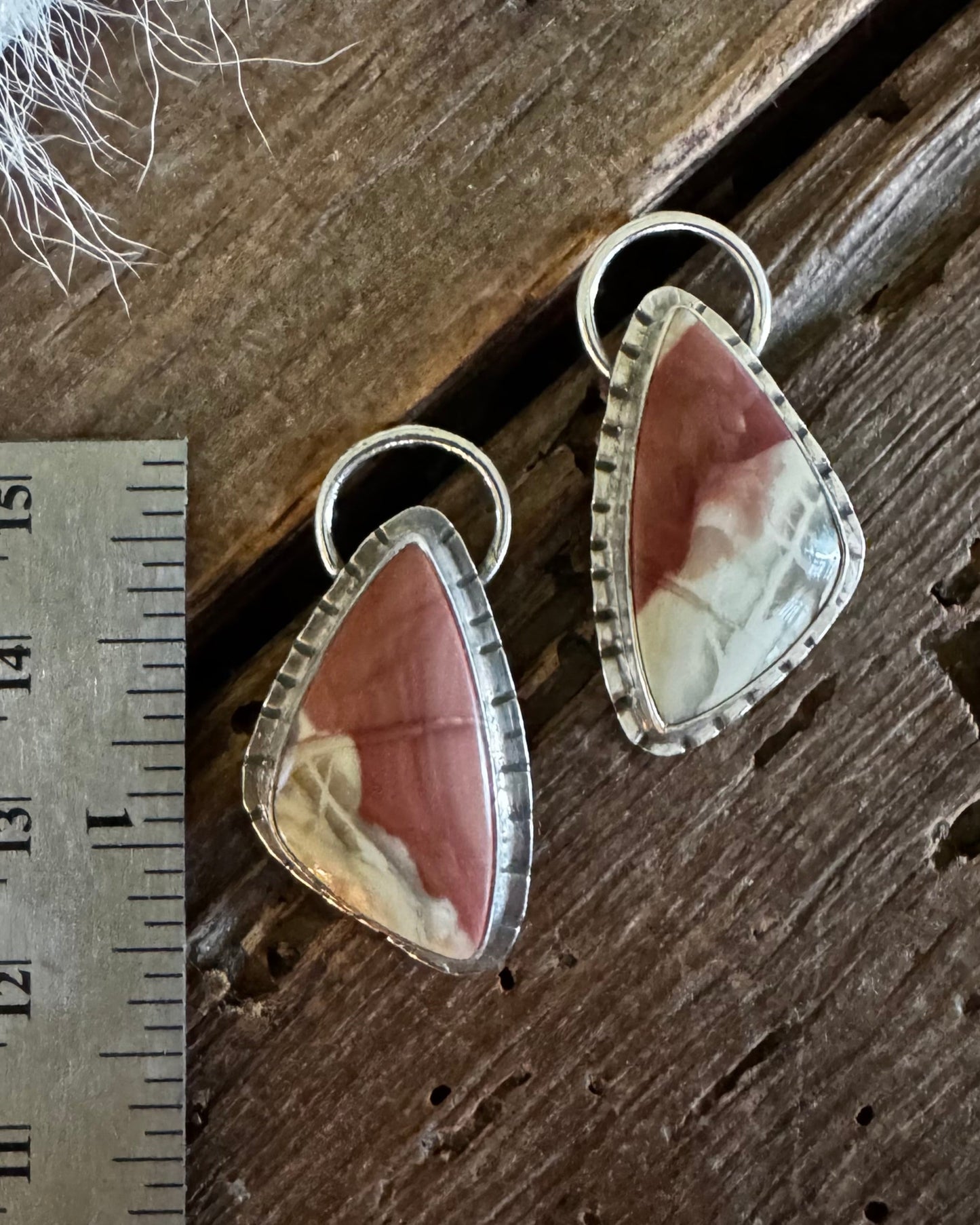 A pair of teardrop-shaped dangle earrings with pinkish-brown and cream marbled stones in silver bezel settings, displayed on a rustic wooden surface next to a metal ruler for scale.