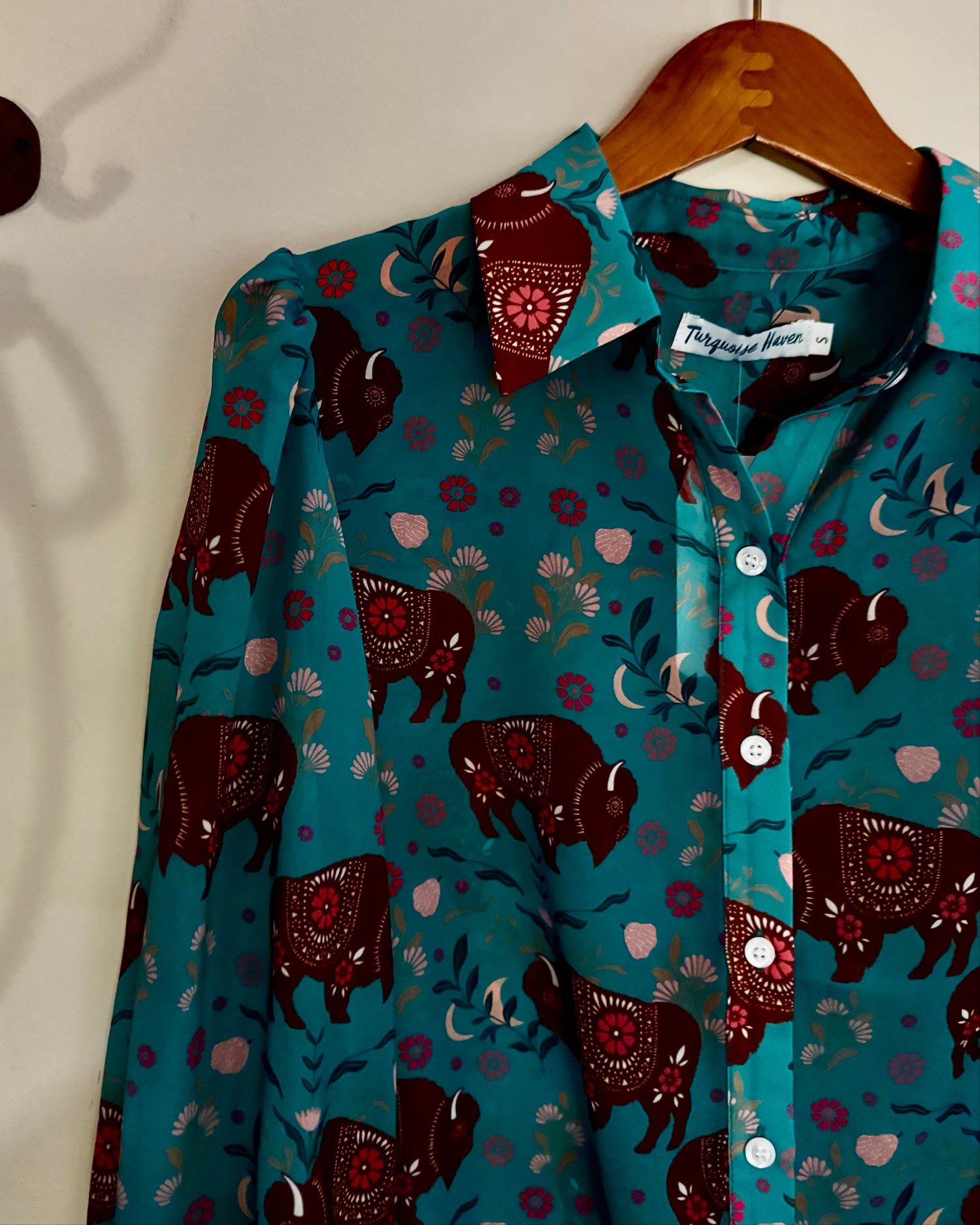 Teal shirt with animal pattern on a hanger against a white wall
