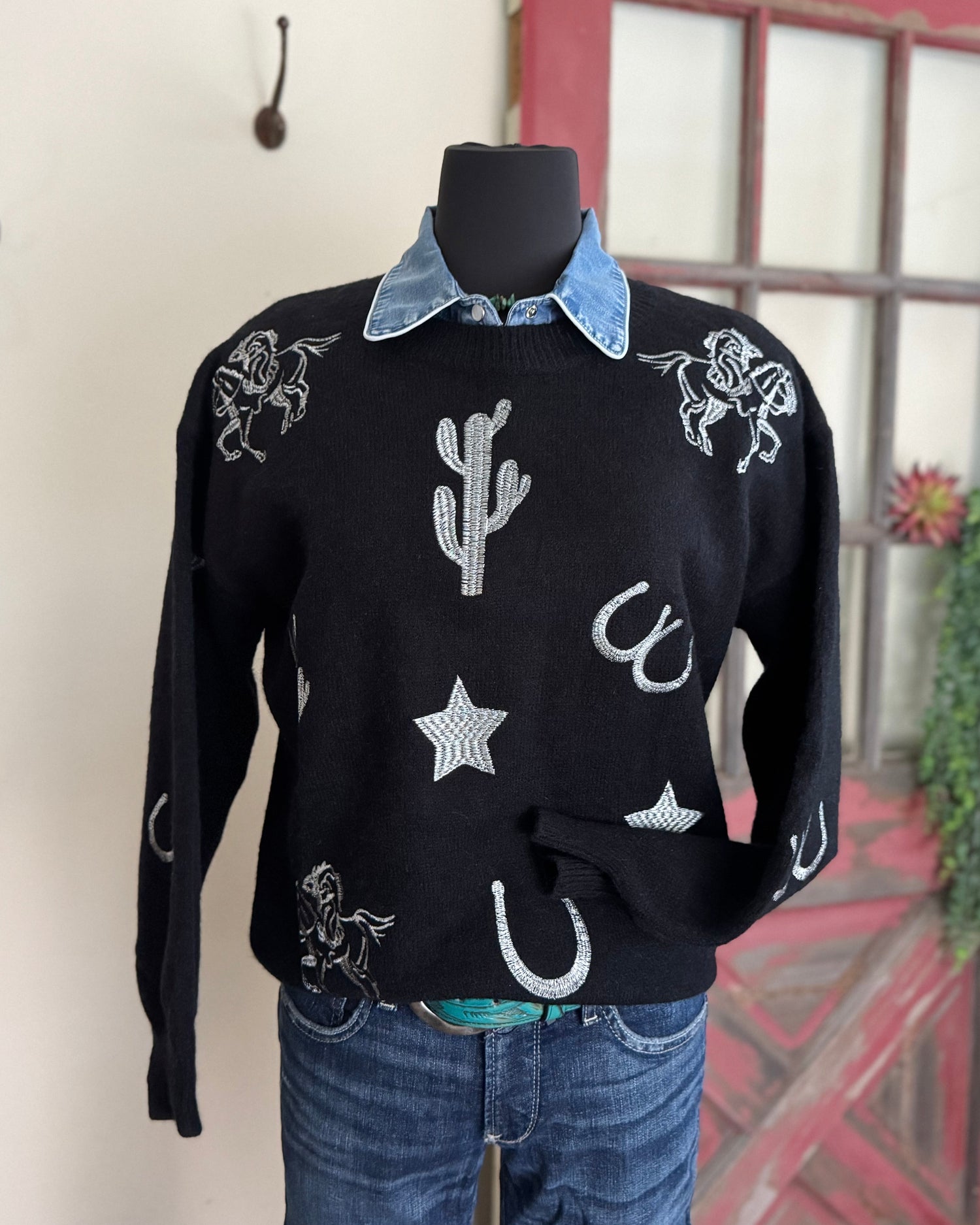 Black sweater with white patterns on a mannequin against a neutral background