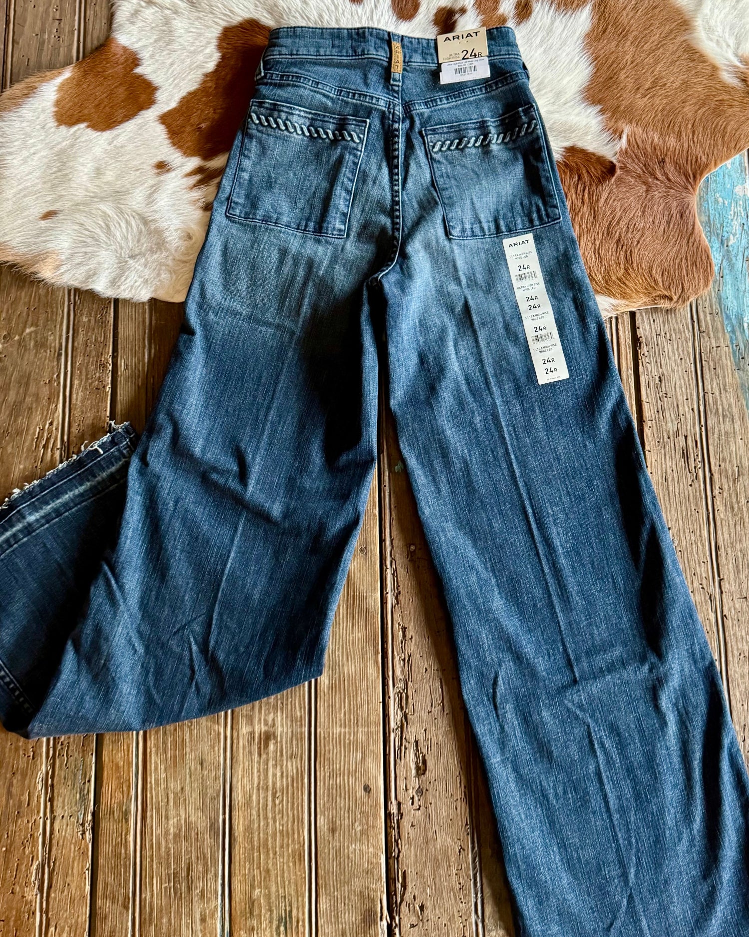 Blue jeans with a tag on a wooden floor and cowhide rug