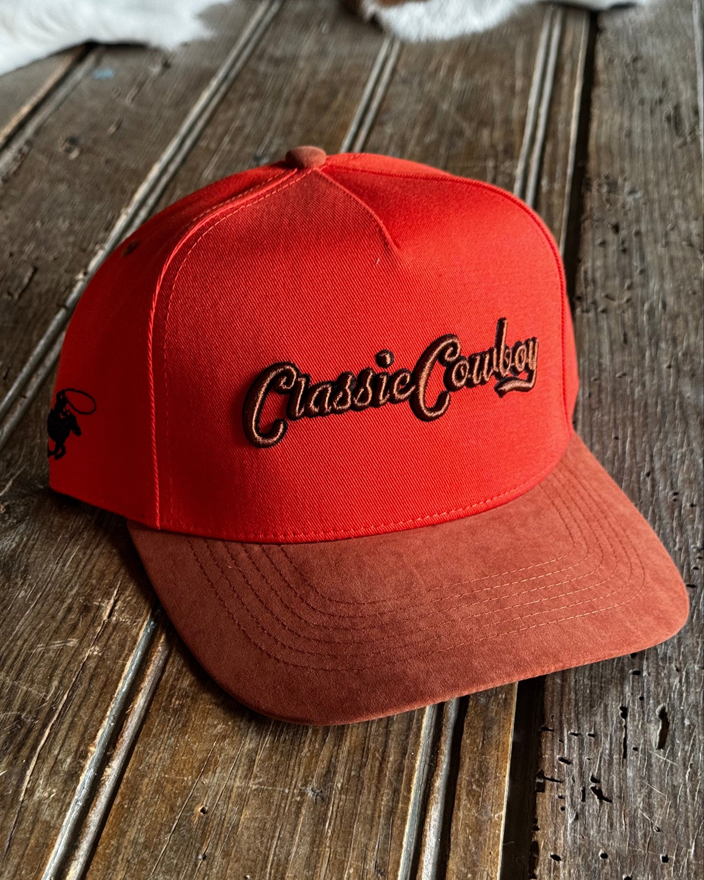 Orange cap with 'Classic Cowboy' logo on a wooden surface