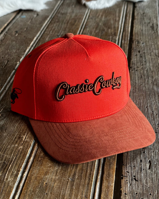Orange cap with 'Classic Cowboy' logo on a wooden surface
