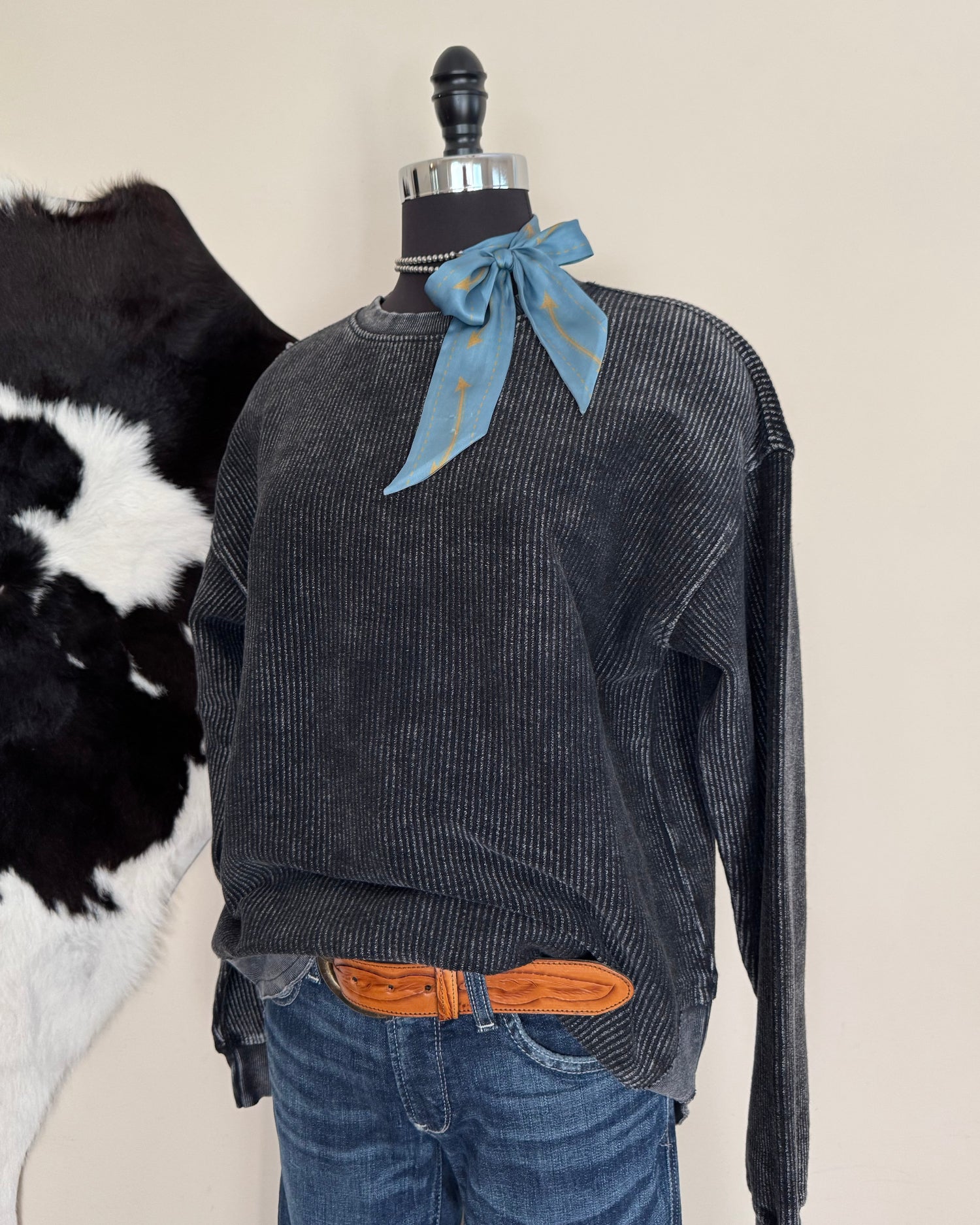 dark grey shirt on mannequin standing on a beige surface with a cowhide rug in the background.
