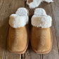 Pair of brown slippers with white fur lining on a wooden surface