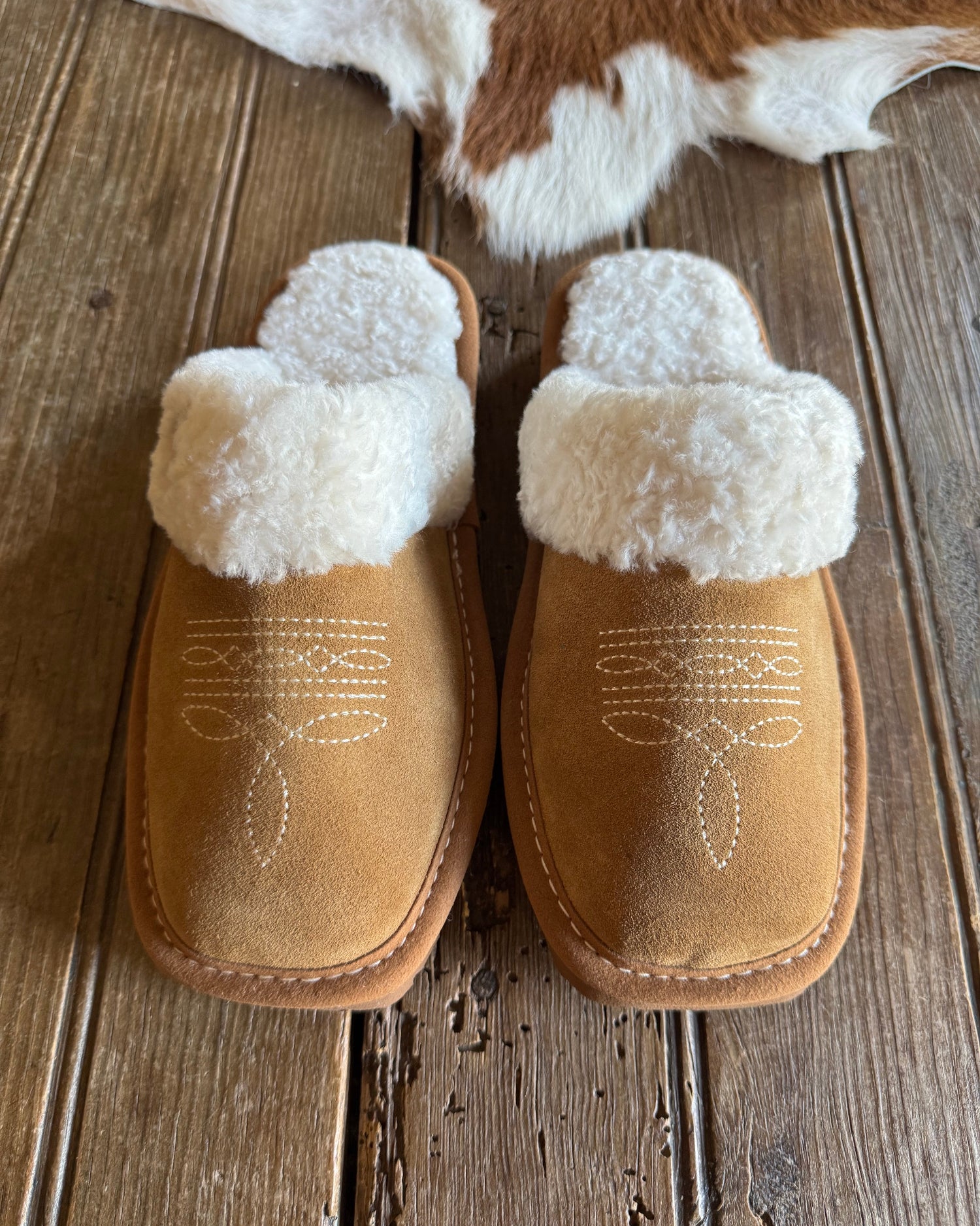 Pair of brown slippers with white fur lining on a wooden surface