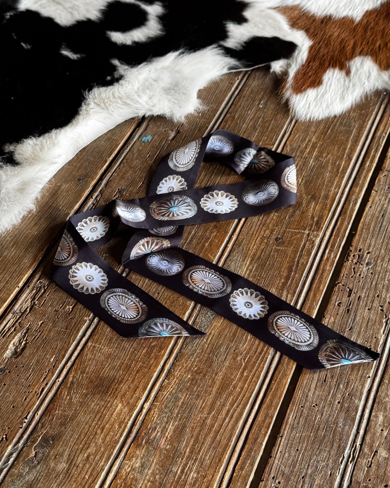Decorative ribbon with circular patterns on a wooden surface next to a cowhide rug