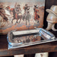 Silver tray on a wooden surface with a book featuring cowboy illustrations in the background.