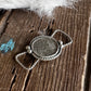 Silver pendant on a wooden surface with white feathers