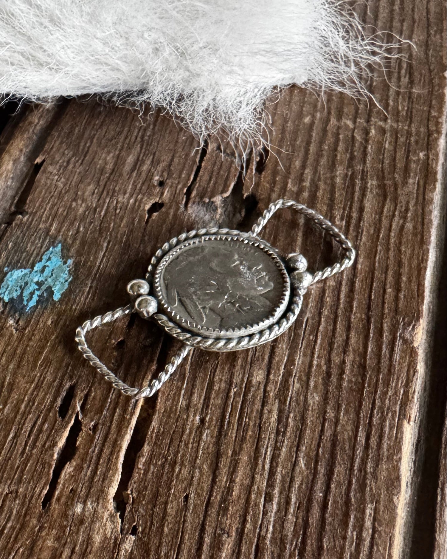 Silver pendant on a wooden surface with white feathers