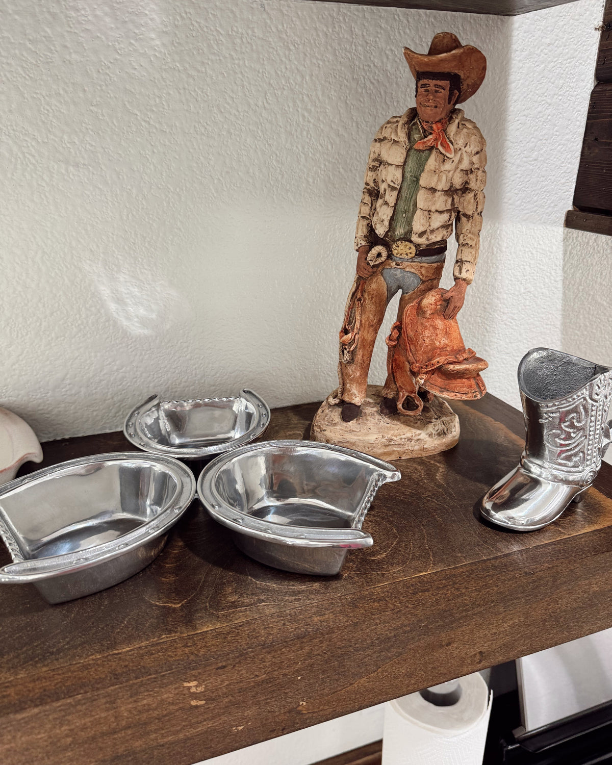 Cowboy figurine with boots and silver bowls on a wooden surface