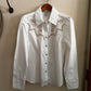 White shirt with lace details on a wooden hanger against a beige wall.