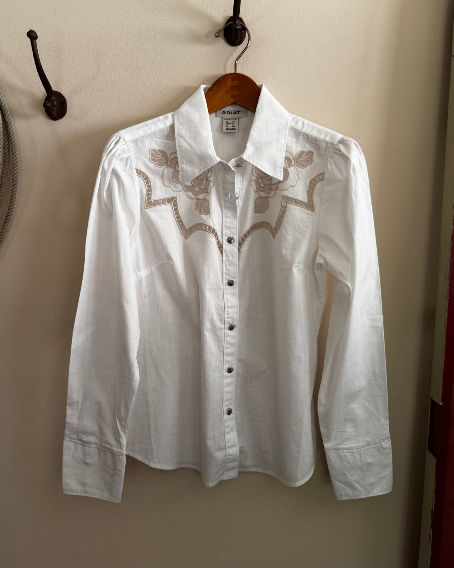 White shirt with lace details on a wooden hanger against a beige wall.