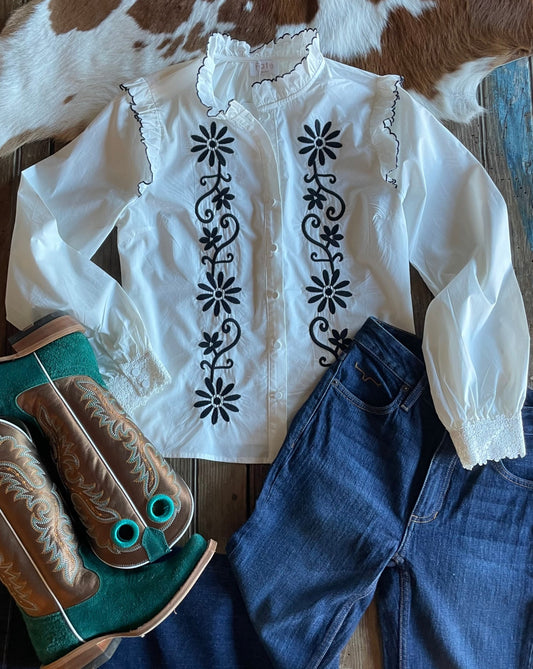 flat lay of white blouse with black embroidery and ruffle details