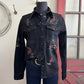 Black denim shirt with embroidery on a mannequin against a rustic background.