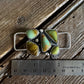 Jewelry piece with green stones on a wooden surface next to a ruler for scale.