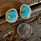 Turquoise stone earrings on a wooden surface with a coin for scale.